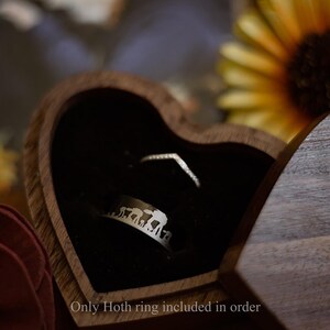 May include: A heart-shaped wooden ring box with a black velvet interior holds two rings. One ring is a silver band with an elephant design, and the other is a delicate, V-shaped ring. The text "Only Hoth ring included in order" is at the bottom.