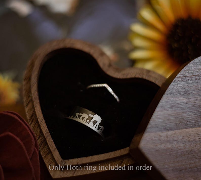 May include: A heart-shaped wooden ring box with a black velvet interior holds two rings. One ring is a silver band with an elephant design, and the other is a delicate, V-shaped ring. The text "Only Hoth ring included in order" is at the bottom.