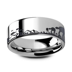 May include: A silver ring with a black etched design depicting a mountain range and figures. The ring has a polished surface and a wide band. The design suggests a science fiction or fantasy theme. The ring's width is approximately 0.8 cm.
