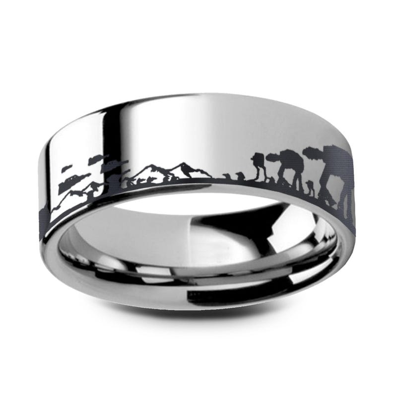 May include: A silver ring with a black etched design depicting a mountain range and figures. The ring has a polished surface and a wide band. The design suggests a science fiction or fantasy theme. The ring's width is approximately 0.8 cm.