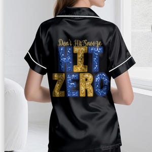 May include: Black satin pajama set with white trim. The top features the text "Don't Hit Snooze" above the words "HIT ZERO" in blue and gold glitter. The set includes a short-sleeved top and matching shorts.