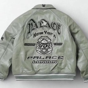 May include: A light grey leather jacket with a white and grey striped hem and cuffs. The back of the jacket features the text "PALACE NEW YORK LONDON TOKYO" in a stylized font, along with a crest and the number "75".