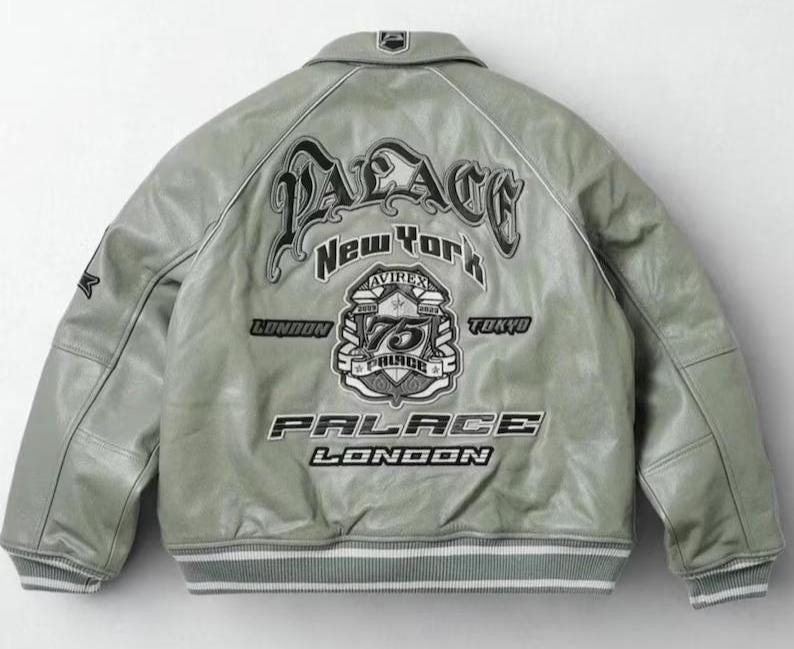 May include: A light grey leather jacket with a white and grey striped hem and cuffs. The back of the jacket features the text "PALACE NEW YORK LONDON TOKYO" in a stylized font, along with a crest and the number "75".