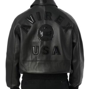 May include: Black leather bomber jacket featuring the word "AVIREX" arched across the back, above a circular emblem and the word "USA". The jacket has a ribbed hem and cuffs, and a classic collar.