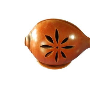 May include: A brown incense burner with a flower-shaped cutout design. The burner has a rounded body and a small spout. The base is a small, circular platform. The incense burner is made of a smooth, glossy material.