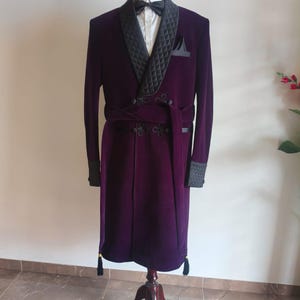 May include: A formal purple velvet robe with a black quilted collar and cuffs. The robe features a matching belt, black tassels, and a black bow tie. The robe is displayed on a wooden mannequin stand.