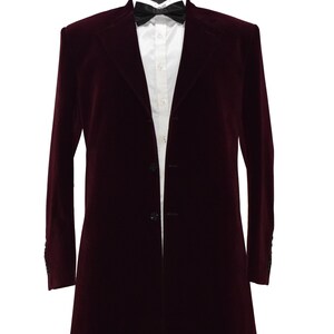 Peut inclure: Un long manteau en velours bordeaux, porté avec une chemise blanche et un nœud papillon noir. Le manteau, présenté sur un mannequin, possède une fermeture à trois boutons. Tenue de soirée pour occasions spéciales.