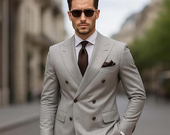 Puede incluir: Un traje gris claro de doble botonadura con corbata y pañuelo de bolsillo marrones. El traje se lleva con una camisa blanca. La persona lleva gafas de sol. El traje tiene un corte clásico.