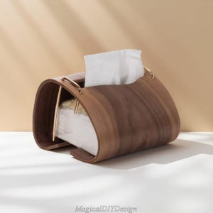 May include: A curved wooden tissue box in dark brown, with gold-coloured metal handles. The box contains white tissues and has the text "MagicalDIYDesign" at the base. The design is modern and stylish.