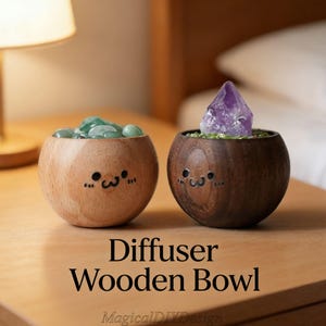 May include: Two wooden bowls with cute faces. One bowl is light-colored and filled with green stones. The other is dark-colored and holds a purple crystal. Text on the surface reads "Diffuser Wooden Bowl".