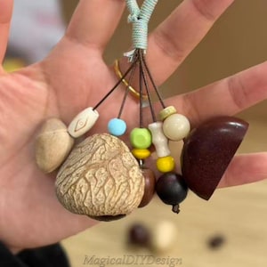 May include: A handcrafted keychain with a selection of natural components and vibrant beads. The keychain incorporates a textured, light brown nut, a dark brown, semi-circular piece, and several small, round beads in various colours. The text "MagicalDIYDesign" is visible.