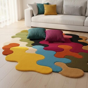 May include: An area rug with an irregular, organic shape featuring a multi-colored pattern of interlocking, blob-like sections in yellow, orange, blue, green, and magenta. Two square, textured throw pillows in teal and magenta rest on the rug.