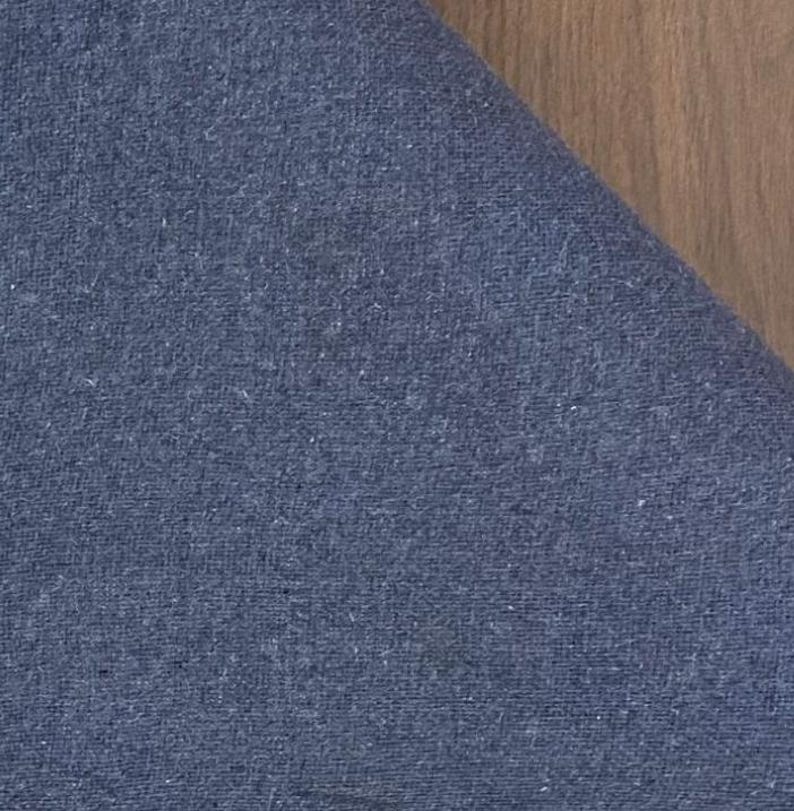May include: A piece of blue fabric with a visible woven texture. The material features a consistent deep blue color throughout, displaying a tight weave pattern with subtle variations in the thread density across the surface of the textile.
