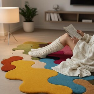 May include: A large, irregular-shaped area rug featuring a vibrant, multi-colored puzzle-piece pattern in shades of mustard yellow, teal, red, olive green, and beige. The rug has a textured, tufted surface and sits flat on a light-colored floor.