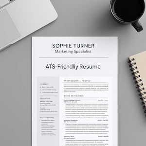 May include: A resume template with the name "Sophie Turner" and the title "Marketing Specialist" at the top. The document is labeled "ATS-Friendly Resume" and includes sections for contact information, education, achievements, and work experience. A black coffee mug and a notebook are on the right.