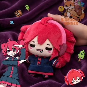 Puede incluir: Un peluche de un personaje con cabello rojo brillante, auriculares rosas y un atuendo azul oscuro con detalles en rojo. El peluche tiene un rostro sencillo con la lengua afuera. Se observa un logotipo de un zorro con el texto SIDEQUEST GINGER.