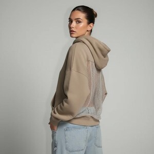 K&ouml;nnte beinhalten: Ein beigefarbener Kapuzenpullover mit Mesh-R&uuml;ckendetail. Der Hoodie hat eine Kapuze mit Kordelzug und eine K&auml;ngurutasche. Das Model tr&auml;gt eine Jeans in heller Waschung. Der Stil ist l&auml;ssig und modern.