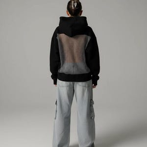 K&ouml;nnte beinhalten: Schwarzer Kapuzenpullover mit Mesh-R&uuml;ckenteil, kombiniert mit hellblauen Cargo-Jeans. Der Kapuzenpullover hat ein klassisches Design mit Kapuze und langen &Auml;rmeln. Die Cargo-Hose hat mehrere Taschen und eine lockere Passform.