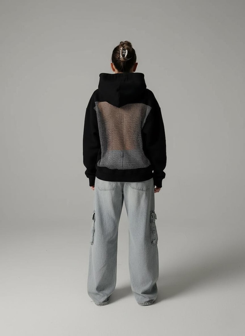 K&ouml;nnte beinhalten: Schwarzer Kapuzenpullover mit Mesh-R&uuml;ckenteil, kombiniert mit hellblauen Cargo-Jeans. Der Kapuzenpullover hat ein klassisches Design mit Kapuze und langen &Auml;rmeln. Die Cargo-Hose hat mehrere Taschen und eine lockere Passform.