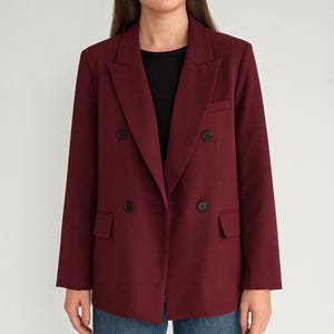 Puede incluir: Una blazer burdeos de doble botonadura con botones negros. La blazer tiene solapas con muescas, dos bolsillos delanteros y un corte clásico a medida. Las mangas son largas y la blazer está hecha de una tela lisa.