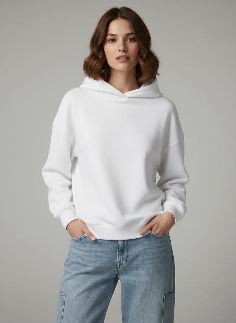 K&ouml;nnte beinhalten: Ein wei&szlig;er Kapuzenpullover mit Kordelzug und langen &Auml;rmeln. Der Pullover ist aus einem weichen Material gefertigt und wird mit hellblauen Jeans kombiniert. Das Model tr&auml;gt den Pullover und die Jeans.