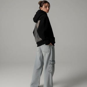 K&ouml;nnte beinhalten: Schwarzer Kapuzenpullover mit Mesh-R&uuml;ckenteil, kombiniert mit hellblauen Cargo-Jeans. Der Kapuzenpullover hat eine Kapuze mit Kordelzug. Die Jeans hat gro&szlig;e Seitentaschen.