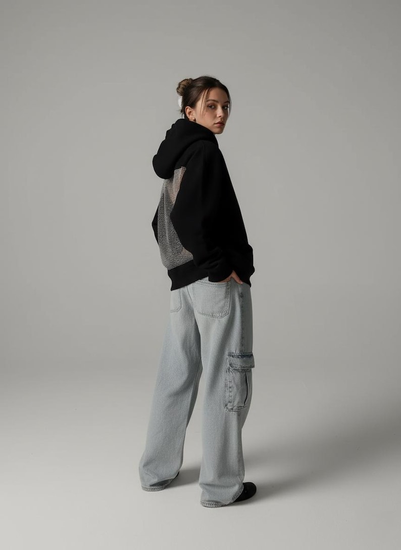 K&ouml;nnte beinhalten: Schwarzer Kapuzenpullover mit Mesh-R&uuml;ckenteil, kombiniert mit hellblauen Cargo-Jeans. Der Kapuzenpullover hat eine Kapuze mit Kordelzug. Die Jeans hat gro&szlig;e Seitentaschen.