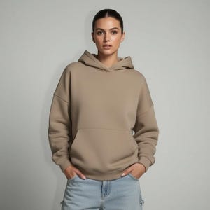 K&ouml;nnte beinhalten: Ein beigefarbener Kapuzenpullover mit K&auml;ngurutasche und Kapuze. Der Hoodie ist aus einem weichen Material gefertigt und wird mit hellblauen Cargo-Jeans kombiniert. Das Model tr&auml;gt den Hoodie und die Jeans.