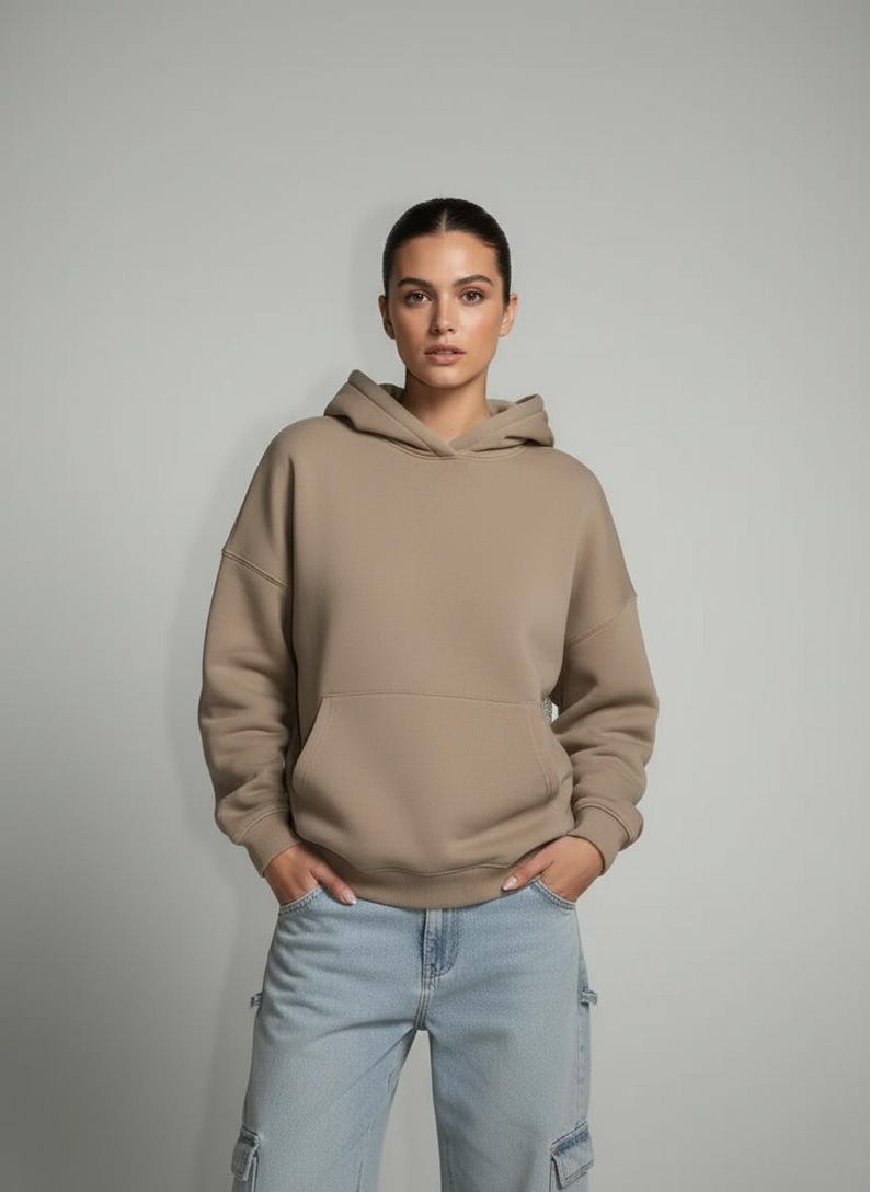 K&ouml;nnte beinhalten: Ein beigefarbener Kapuzenpullover mit K&auml;ngurutasche und Kapuze. Der Hoodie ist aus einem weichen Material gefertigt und wird mit hellblauen Cargo-Jeans kombiniert. Das Model tr&auml;gt den Hoodie und die Jeans.