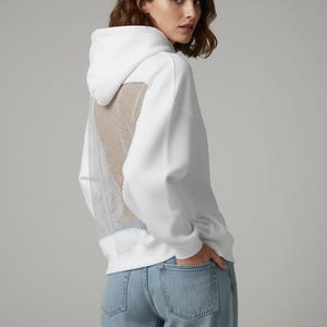 K&ouml;nnte beinhalten: Wei&szlig;er Kapuzenpullover mit Mesh-R&uuml;ckenteil. Der Hoodie hat eine Kapuze mit Kordelzug und lange &Auml;rmel. Das Model tr&auml;gt hellblaue Jeans. Der Mesh-R&uuml;cken verleiht dem l&auml;ssigen Sweatshirt ein einzigartiges Designelement.