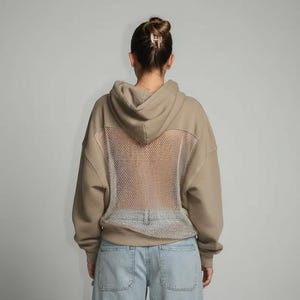 K&ouml;nnte beinhalten: Beigefarbener Kapuzenpullover mit Mesh-R&uuml;ckenteil. Der Hoodie hat eine Kapuze mit Kordelzug und lange &Auml;rmel. Das Model tr&auml;gt hellblaue Jeans. Der Mesh-R&uuml;cken verleiht dem l&auml;ssigen Sweatshirt ein einzigartiges Designelement.