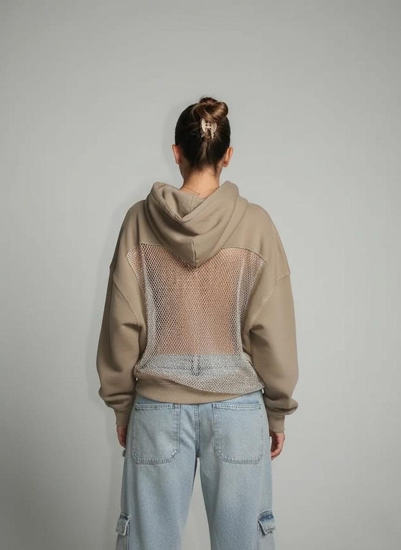 K&ouml;nnte beinhalten: Beigefarbener Kapuzenpullover mit Mesh-R&uuml;ckenteil. Der Hoodie hat eine Kapuze mit Kordelzug und lange &Auml;rmel. Das Model tr&auml;gt hellblaue Jeans. Der Mesh-R&uuml;cken verleiht dem l&auml;ssigen Sweatshirt ein einzigartiges Designelement.