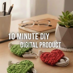 Op de afbeelding: Op een houten bureau worden drie handgemaakte, hartvormige oortelefoonhouders van haakwerk in groen en rood getoond, elk met witte oortelefoons. De tekst luidt "10 MINUTE DIY DIGITAL PRODUCT."