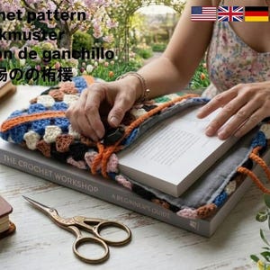 May include: A crochet project with a book titled "The Crochet Workshop" and a pair of gold scissors. The project is a colorful granny square design with blue, orange, and cream colors. The book is open, and the project is placed on top.