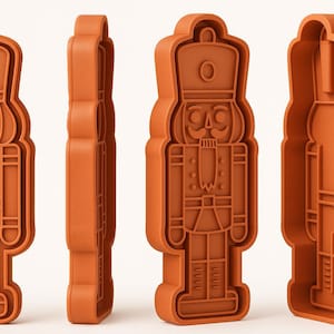 Può includere: Tagliapasta in plastica arancione a forma di soldato schiaccianoci. Il tagliapasta presenta dettagli come cappello, baffi e uniforme. L'immagine mostra il tagliapasta da più angolazioni.