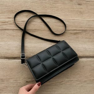 以下が含まれることがあります： キルティングデザインの黒いクロスボディバッグ。 長く調整可能なストラップとシルバーカラーのバックルが付いています。 長方形のバッグにはフラップクロージャーが付いています。 素材は滑らかです。