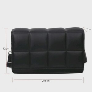 以下が含まれることがあります： 黒色のキルティングクロスボディバッグ。バッグは長方形で、パッド入りの格子状のデザインです。長さ20.5cm、高さ12cm、幅7cmです。長い調節可能なストラップとフラップクロージャーが付いています。