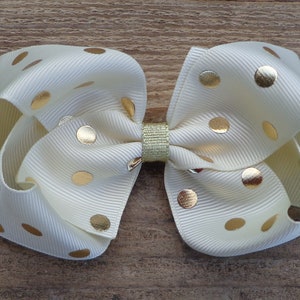 May include: A white bow with gold polka dots. The bow is made of a soft, textured fabric and has a gold glitter center.