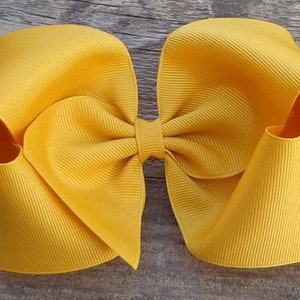 May include: A large, bright yellow hair bow made from grosgrain ribbon. The bow is tied in a classic, symmetrical shape with two loops and a center knot.
