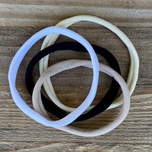 May include: Four hair ties in different colors: light blue, beige, black, and white. The hair ties are made of soft, stretchy fabric and are perfect for holding back hair.
