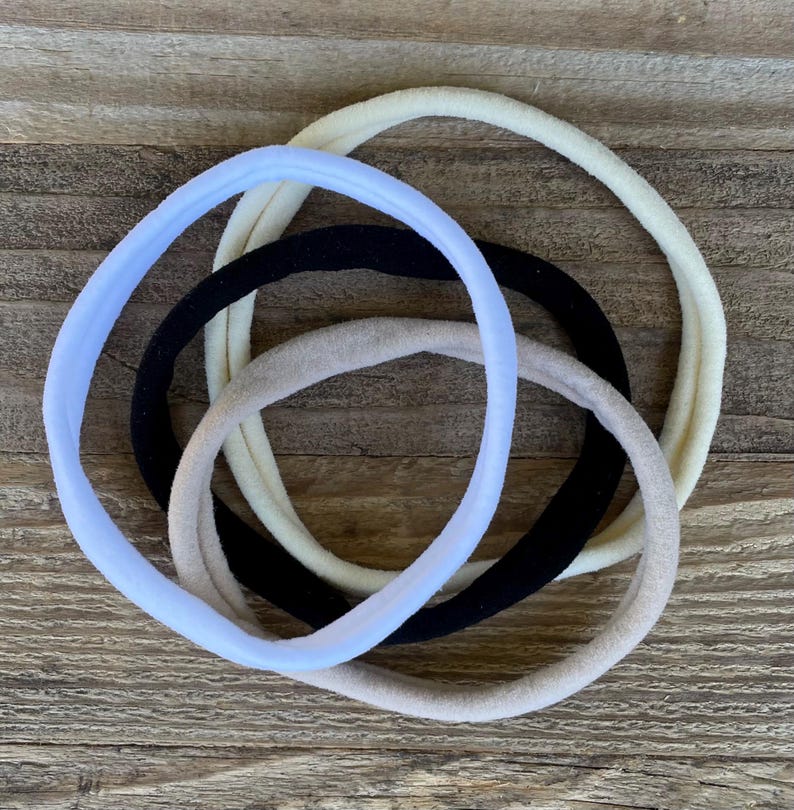 May include: Four hair ties in different colors: light blue, beige, black, and white. The hair ties are made of soft, stretchy fabric and are perfect for holding back hair.