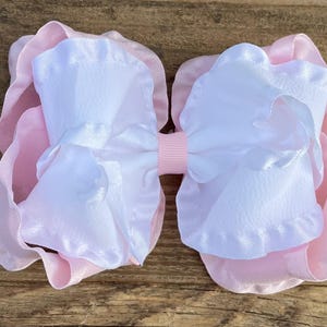 May include: A large pink and white satin bow with ruffled edges. The bow is made of two layers of fabric, with the top layer being white and the bottom layer being pink.
