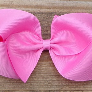 May include: A large pink bow made from grosgrain ribbon. The bow is tied with a small piece of ribbon in the center.