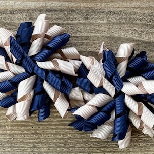 May include: Two hair clips with a navy blue and cream ribbon twist design.