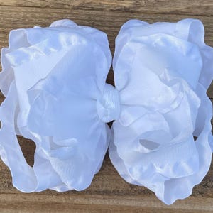 May include: A large white satin bow with ruffled edges. The bow is made of two layers of fabric and has a center knot.