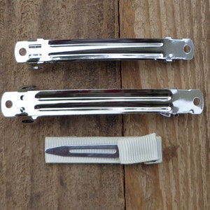 May include: Two silver metal hair clips and a white ribbon hair tie. The hair clips are about 2 inches long and have a smooth, shiny finish.