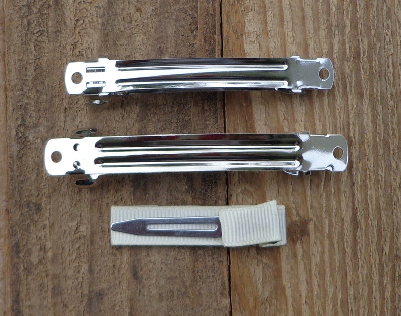 May include: Two silver metal hair clips and a white ribbon hair tie. The hair clips are about 2 inches long and have a smooth, shiny finish.