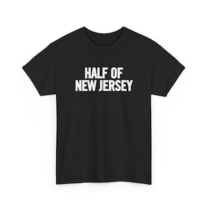 Puede incluir: Camiseta negra con el texto blanco "HALF OF NEW JERSEY" impreso en el pecho. El texto está en negrita, sin serifa. La camiseta tiene mangas cortas y cuello redondo.