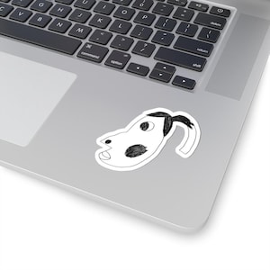 May include: A white sticker depicting a quirky, hand-drawn dog's head with black details and a curved tail. The dog has a large eye, a spot, and a smiling mouth. The sticker is on a laptop.