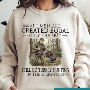 May include: Sand-colored sweatshirt with the text "ALL MEN ARE CREATED EQUAL ONLY THE BEST STILL GO TURKEY HUNTING IN THEIR EIGHTIES." A hunter with a rifle and a turkey are in the graphic. The words "SUPER SOFT" are in a pink heart.